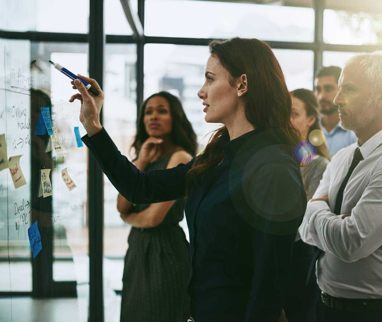 A woman presenting ideas on a glass board to colleagues in a modern office.