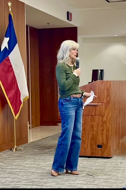 Woman speaking at a podium with a Texas flag in the background.